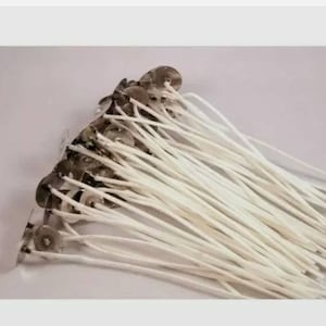 May include: A collection of candle wicks with metal bases. The wicks are white and appear to be made of cotton. The metal bases are silver and circular. The wicks are arranged in a bundle.