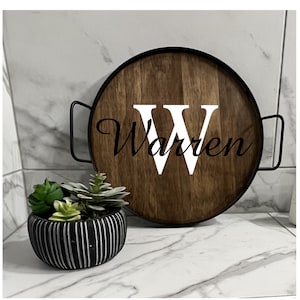 May include: A round wooden tray with black metal handles. The tray has a white letter "W" and the name "Warren" written in black cursive lettering.