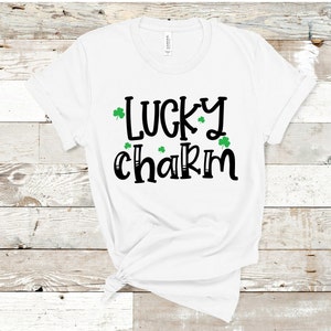 May include: White t-shirt with black text that reads "lucky charm" and green shamrock graphics.