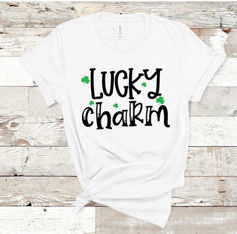 May include: White t-shirt with black text that reads "lucky charm" and green shamrock graphics.