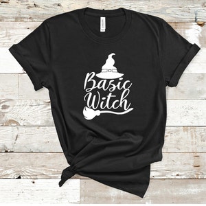 May include: Black t-shirt with the words "Basic Witch" in white script, accompanied by a witch hat and broom graphic. The shirt is made of a soft material and is perfect for Halloween or everyday wear.