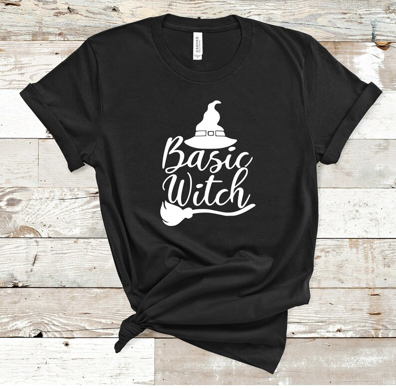 May include: Black t-shirt with the words "Basic Witch" in white script, accompanied by a witch hat and broom graphic. The shirt is made of a soft material and is perfect for Halloween or everyday wear.