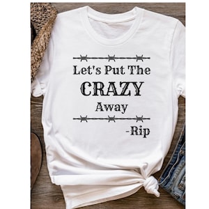May include: White t-shirt with black text that reads "Let's Put The CRAZY Away -Rip" with barbed wire accents.