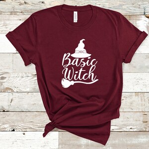 May include: A maroon t-shirt with the words "Basic Witch" in white script, along with a witch hat and broom graphic. The shirt is made of a soft material and is perfect for Halloween.