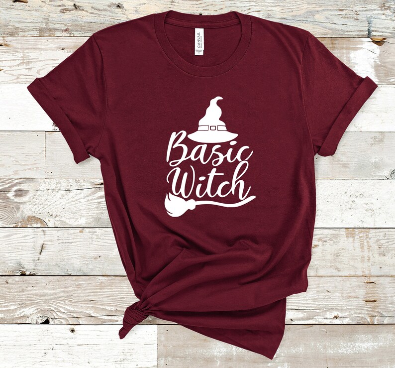 May include: A maroon t-shirt with the words "Basic Witch" in white script, along with a witch hat and broom graphic. The shirt is made of a soft material and is perfect for Halloween.