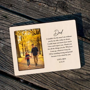 May include: A wooden picture frame with a photograph of a father and child walking in a park. The frame includes the text "Dad" and a heartfelt message. The frame is resting on a weathered wooden surface.