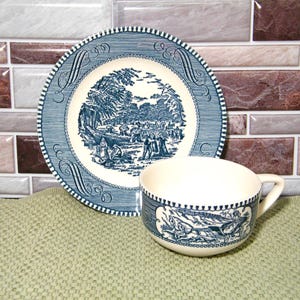 May include: A blue and white ceramic plate and teacup set. The plate and teacup feature a detailed landscape scene in blue. The plate has a decorative border. The teacup has a handle and a matching design.