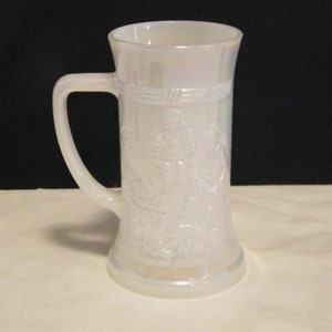 May include: A white iridescent glass mug featuring a raised relief design of figures around the exterior. The mug has a smooth cylindrical body, a flared rim, and a sturdy handle on the side. The glass surface displays a pearlescent sheen.