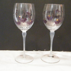 Puede incluir: Dos copas de vino transparentes con diseño floral morado y detalles dorados. Las copas tienen un tallo largo y una base redonda. Perfectas para servir vino en ocasiones especiales.