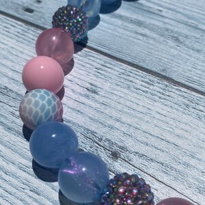 May include: A colorful beaded necklace with pink, blue, and iridescent beads. The beads are arranged in a pattern and have a variety of textures.