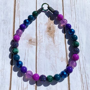 May include: A colorful beaded necklace with shades of purple, pink, blue, and green. The beads are round and have a glossy finish.