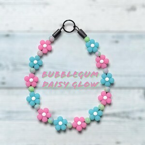 May include: A necklace featuring pink and blue daisy flower beads, with light green and white beads. The necklace has a black clasp and the text "BUBBLEGUM DAISY GLOW" in the center.