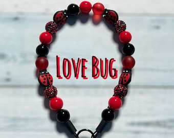 May include: A red and black beaded necklace with ladybug charms and the text "LOVE BUG".