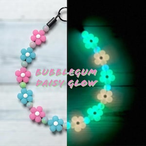 May include: A necklace with pink and blue daisy flower beads with white centres, and light pink and green beads. The text "BUBBLEGUM DAISY GLOW" is visible. The necklace glows in the dark.
