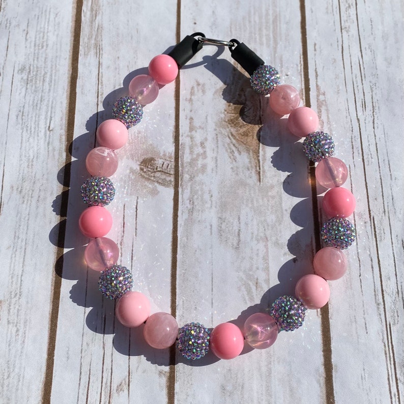 May include: A pink and silver beaded necklace with a clasp closure. The beads are made of various materials, including glass, crystal, and metal.