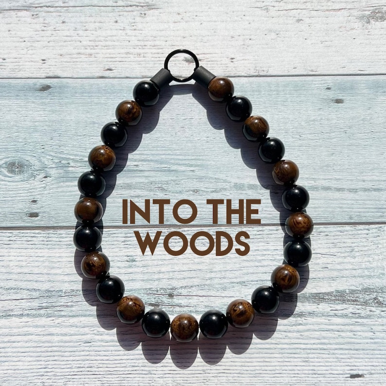 May include: A brown and black beaded necklace with a metal ring clasp. The necklace has the text "INTO THE WOODS" printed on it.