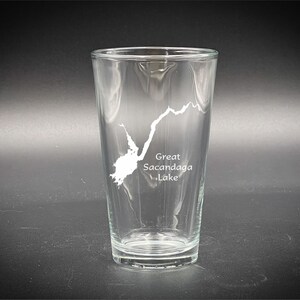 May include: A clear glass pint glass with a white outline of Great Sacandaga Lake etched on the side.