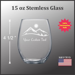 May include: A clear, stemless wine glass with a mountain and sun design. The glass is 4 1/2 inches tall and holds 15 oz. The text "Your Custom Text" is displayed on the glass. Dishwasher safe. Made in the USA.