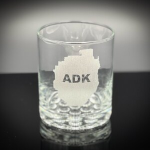 May include: A clear glass tumbler with an etched design of the Adirondack Mountains and the text "ADK".