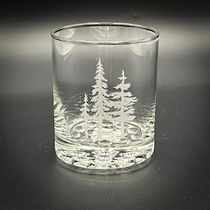 May include: A clear glass tumbler with an etched design of three pine trees. The glass has a textured bottom.