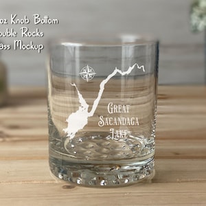 May include: A clear glass tumbler with a knob bottom and double rocks design. The glass features a white graphic of Great Sacandaga Lake, a compass rose, and text that reads "Great Sacandaga Lake". The glass is 12.25 oz.
