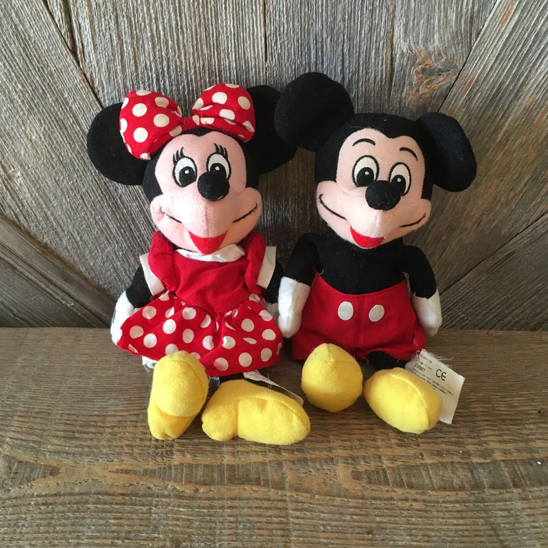 K&ouml;nnte beinhalten: Ein Paar Pl&uuml;schtiere von Mickey Mouse und Minnie Mouse. Mickey tr&auml;gt rote Shorts und schwarze Schuhe. Minnie tr&auml;gt ein rotes Kleid mit wei&szlig;en Punkten und gelbe Schuhe. Beide haben schwarze Augen und einen roten Mund.