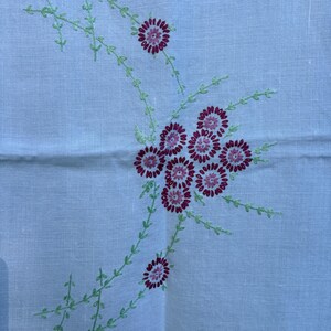 May include: A light blue linen textile with embroidered floral design. The embroidery features clusters of burgundy flowers with green stems and leaves. The textile has a subtle texture and a vintage aesthetic.