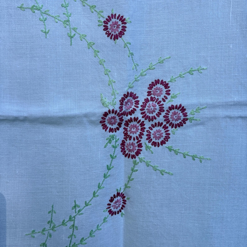 May include: A light blue linen textile with embroidered floral design. The embroidery features clusters of burgundy flowers with green stems and leaves. The textile has a subtle texture and a vintage aesthetic.