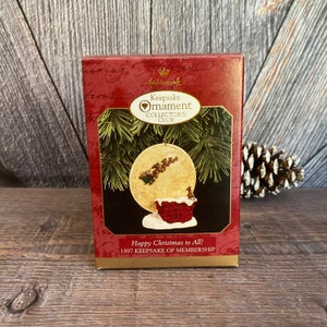 May include: A red and white box with a Hallmark Keepsake Ornament Collector's Club logo. The box features a picture of a Santa Claus ornament with a red brick chimney and a white moon in the background. The text on the box reads "Happy Christmas to All! 1997 Keepsake of Membership."