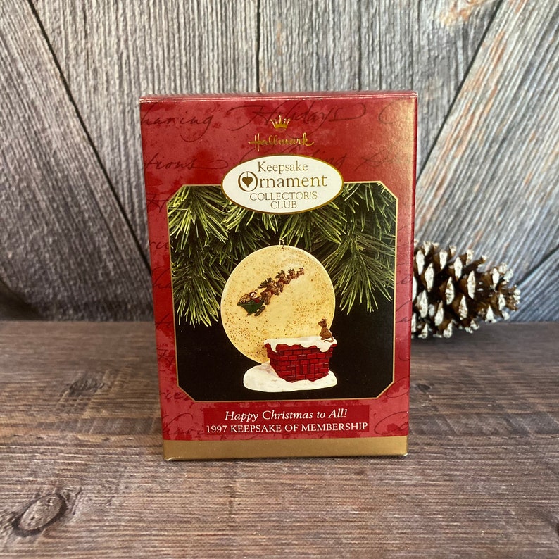 May include: A red and white box with a Hallmark Keepsake Ornament Collector's Club logo. The box features a picture of a Santa Claus ornament with a red brick chimney and a white moon in the background. The text on the box reads "Happy Christmas to All! 1997 Keepsake of Membership."