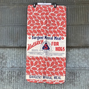 May include: A vintage feed bag with a red and white leaf pattern. The bag is labeled "Sargent Minral Meal MultiRich For Hogs".