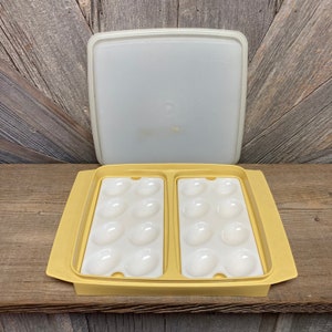 May include: A vintage yellow and white egg container with a lid. The container has two sections, each holding six egg-shaped indentations. The lid is off, revealing the interior. The container is made of plastic.