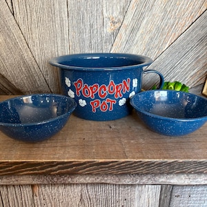 May include: A blue enamel popcorn pot with a handle and two matching bowls. The pot has the words "Popcorn Pot" in red lettering with white popcorn graphics. The bowls and pot have a speckled design.