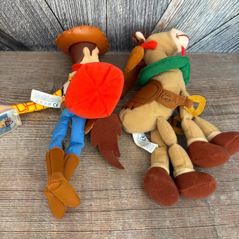 May include: Two plush toys from the animated film Toy Story. One is Woody, a cowboy doll with a brown hat, red vest, blue pants, and brown boots. The other is a horse with a green hat and brown saddle.