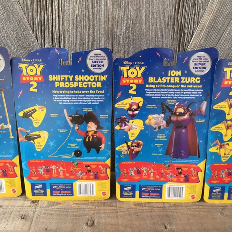 May include: Four Toy Story 2 action figure packages. The packages feature characters like Shifty Shootin' Prospector and Ion Blaster Zurg. Each package has a blue background with yellow accents and character illustrations. The text "Silver Edition" is visible on each package.