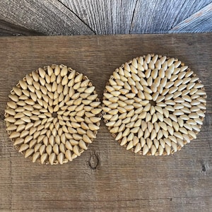 May include: Two round coasters made of natural beige seashells arranged in a circular pattern. The coasters are set on a wooden surface.