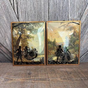 May include: Two framed silhouette art pieces. One depicts a couple on a swing, the other a couple walking in a landscape. Both have gold frames and are set against a scenic background.
