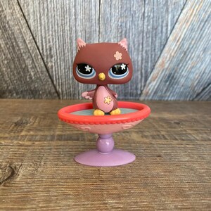 May include: A brown owl with blue eyes and pink flowers on its chest is standing on a pink and red pedestal with a blue base.