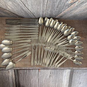 May include: A collection of vintage silverware, including knives, forks, and spoons, arranged on a wooden surface. The silverware is made of a shiny, silver-colored metal. The arrangement suggests a formal dining setting, perfect for a special occasion.