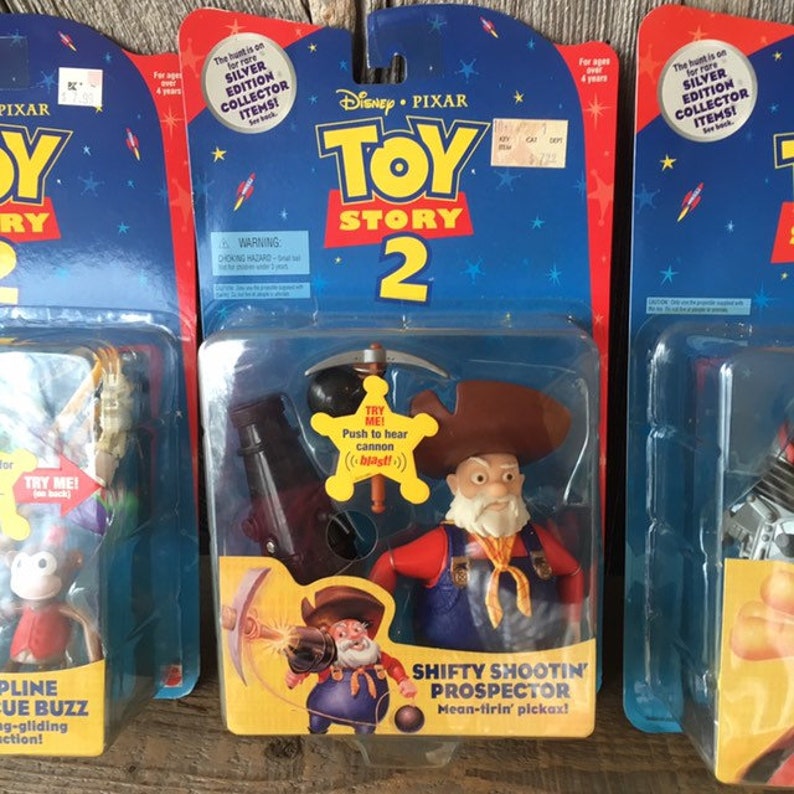 May include: Collectible Toy Story 2 action figures in original packaging. The Shifty Shootin' Prospector figure is in the center, with a brown hat, red shirt, and blue overalls. The packaging features the Disney Pixar logo and the text "Silver Edition Collector Items!"