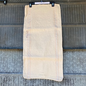 May include: A vintage white linen sack with red and blue stripes. The sack has the text "247/9" and "7X-20" printed on it.