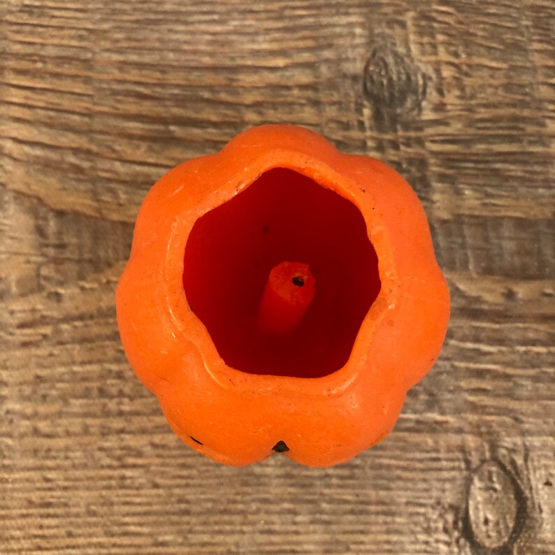 May include: Orange pumpkin-shaped candle with a hollow center and a small wick.