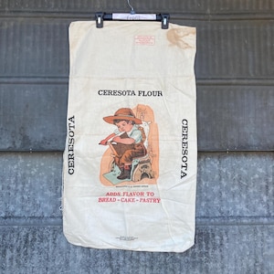 May include: Vintage white flour sack with a red and black illustration of a child holding a book. The sack has the text "Ceresota Flour" and "Adds Flavor to Bread - Cake - Pastry" printed on it.