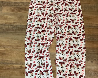May include: White pajama pants with a repeating pattern of a cartoon woman, red lips, and the word "Boop" in red. The pants have a drawstring waist and a relaxed fit.