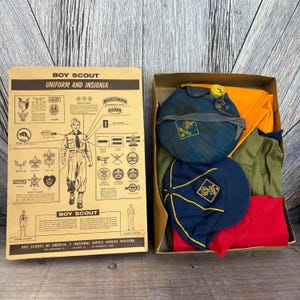 May include: Vintage Boy Scout uniform and insignia set. The box contains a blue cap, canteen, and uniform pieces in green and red. The box also includes a guide to the uniform and insignia.
