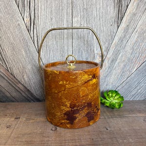 May include: A vintage ice bucket with a gold-tone handle and a marbled brown and gold finish.