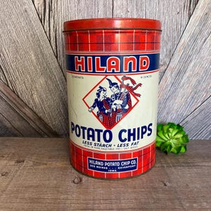 May include: Vintage Hiland Potato Chips tin with a red and blue plaid pattern. The tin features the words "Hiland Potato Chips" and a graphic of two people in Scottish attire. The tin is 16 ounces.