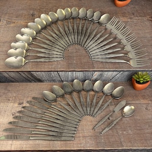 May include: Arrangement of vintage silverware, including spoons, forks, knives, and butter knives, displayed on a wooden surface. The silverware has a decorative pattern on the handles. The spoons, forks, and knives are arranged in a fan shape.