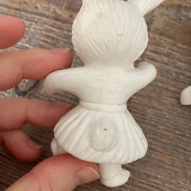May include: White ceramic bunny figurine with a skirt and a tail. The figurine is marked "Made in Hong Kong".