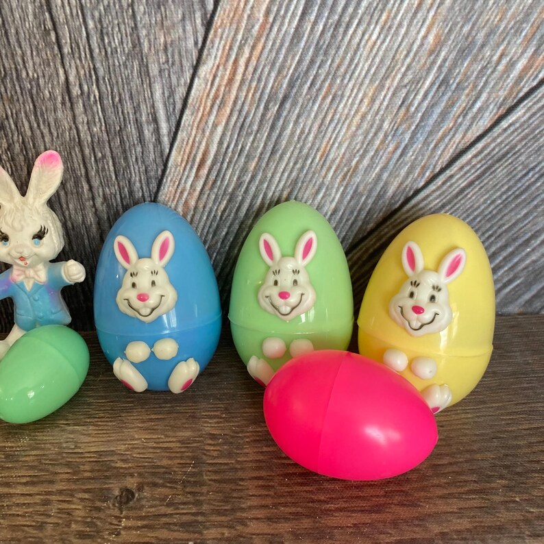 May include: Five plastic Easter eggs with bunny faces. The eggs are in blue, green, yellow, and pink.